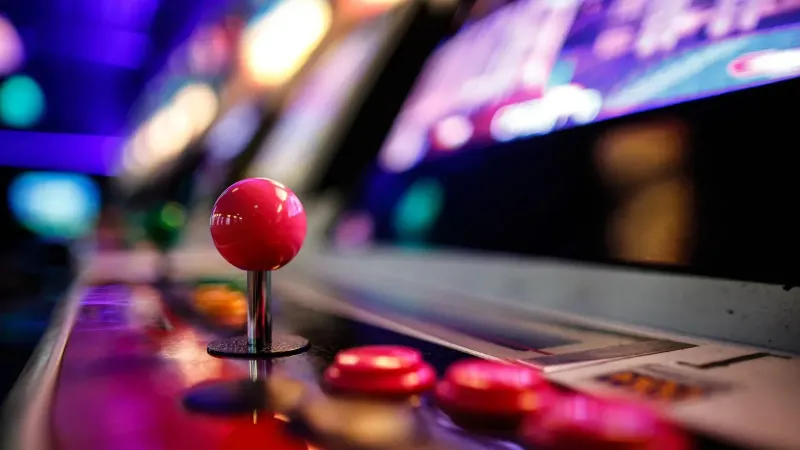 Close-up de un vibrante joystick de arcade retro y botones con luces borrosas en el fondo.