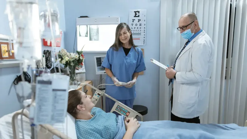 Un médico y una enfermera atendiendo a una paciente en una habitación de hospital.