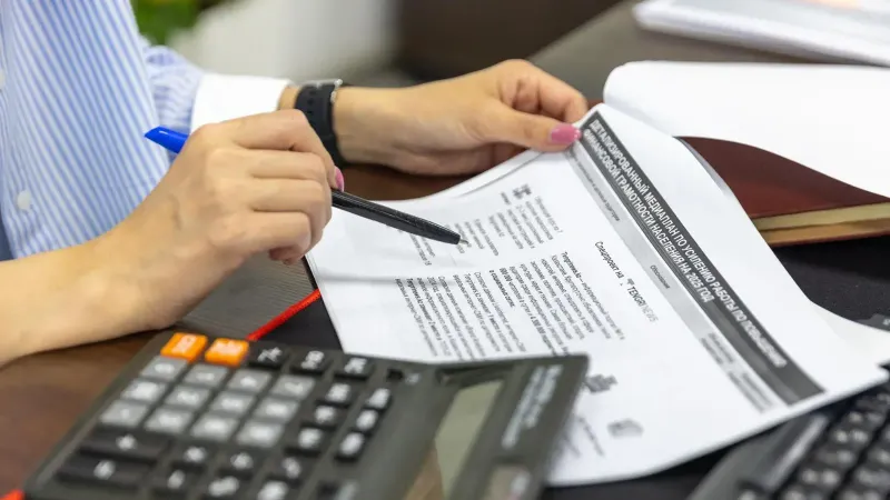 Primer plano de una persona que analiza documentos financieros usando una calculadora y un bolígrafo.