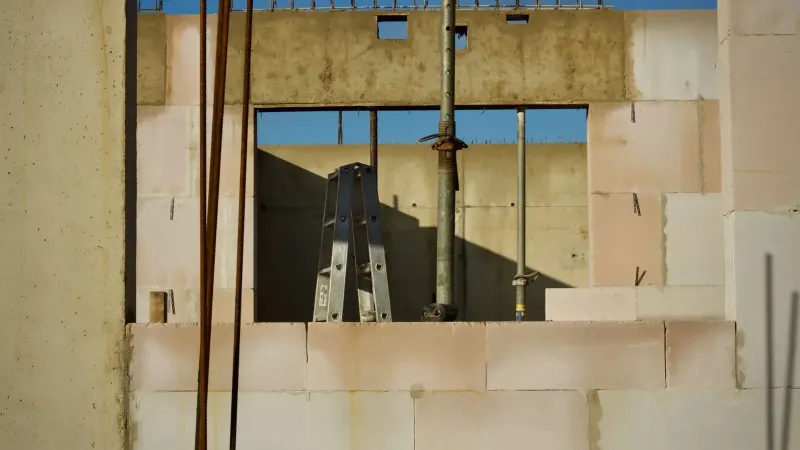 Vista de un sitio de construcción con paredes de hormigón y escalera de metal bajo un cielo azul.