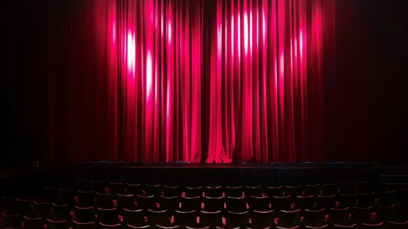 Empty theater stage with red curtains and seating, ready for a performance.