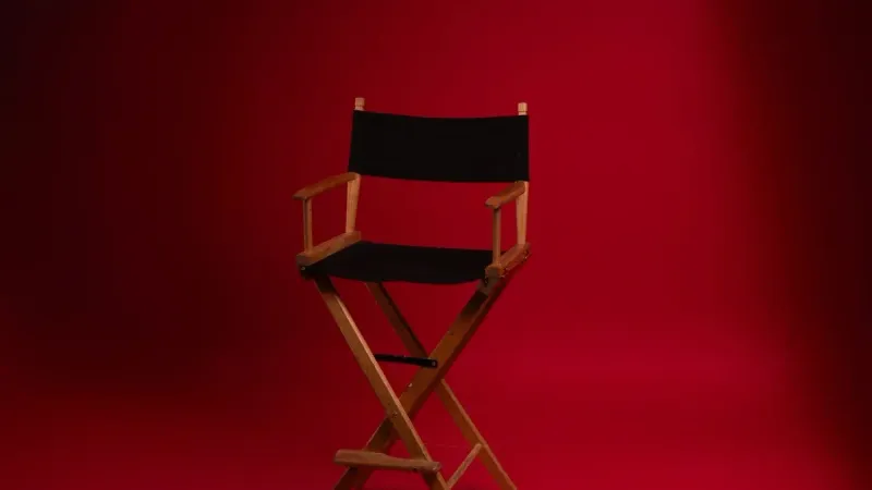 A wooden director's chair against a vibrant red backdrop, symbolizing film industry authority.