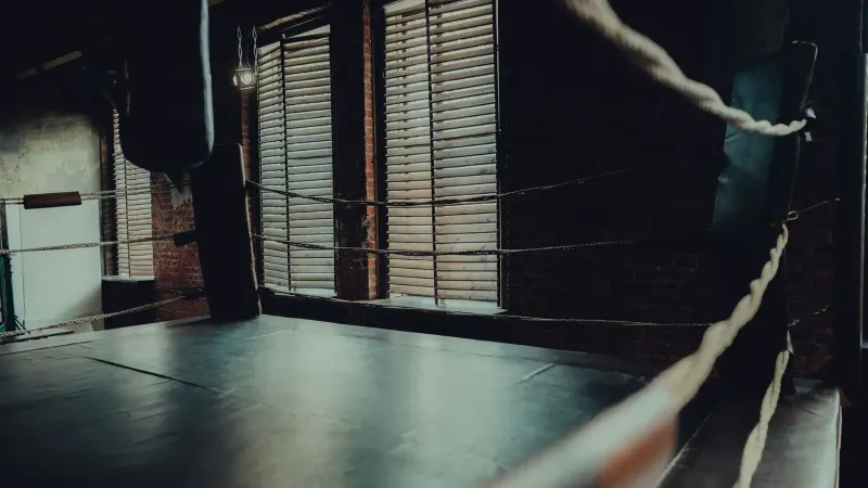 Anillo de boxeo vacío en un gimnasio atmosférico con iluminación de mal humor y paredes de ladrillo.