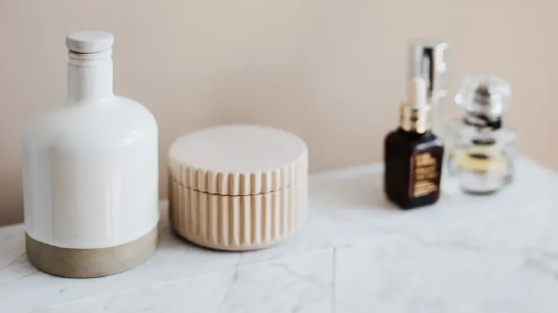 Conjunto de envases cosméticos reutilizables para crema y champú dispuestos cerca de varios productos para el cuidado de la piel y botella de perfume en estante de mármol blanco contra la