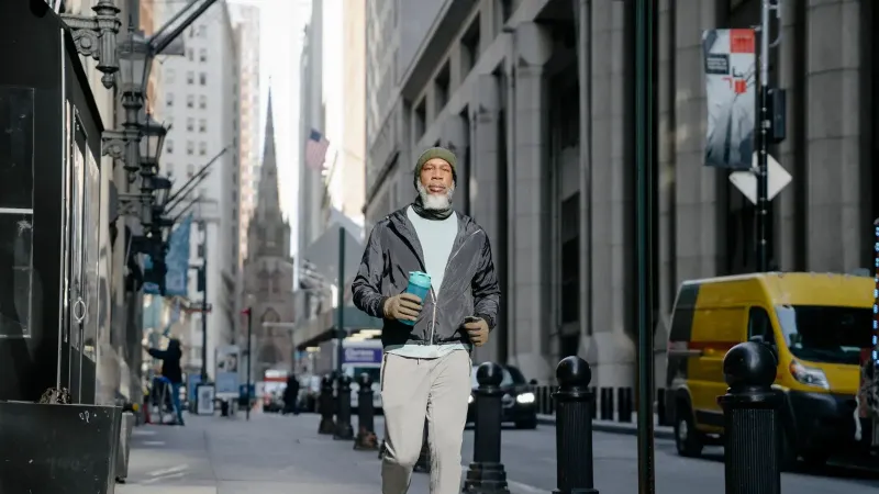 Hombre mayor con ropa activa llevando una botella de agua mientras camina en una bulliciosa calle de la ciudad.