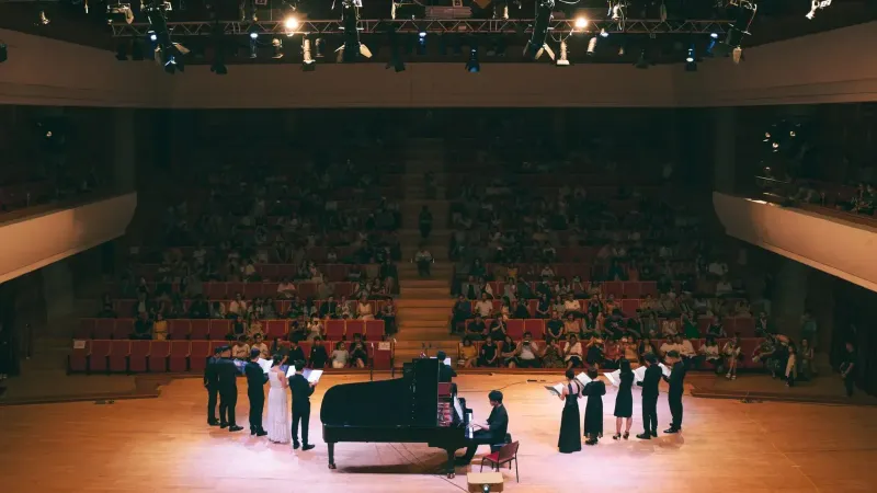 Concierto de música clásica vibrante con pianista y cantantes en el escenario.