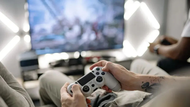 Manos sosteniendo un controlador de videojuegos en una moderna sala de estar, jugando en la televisión.