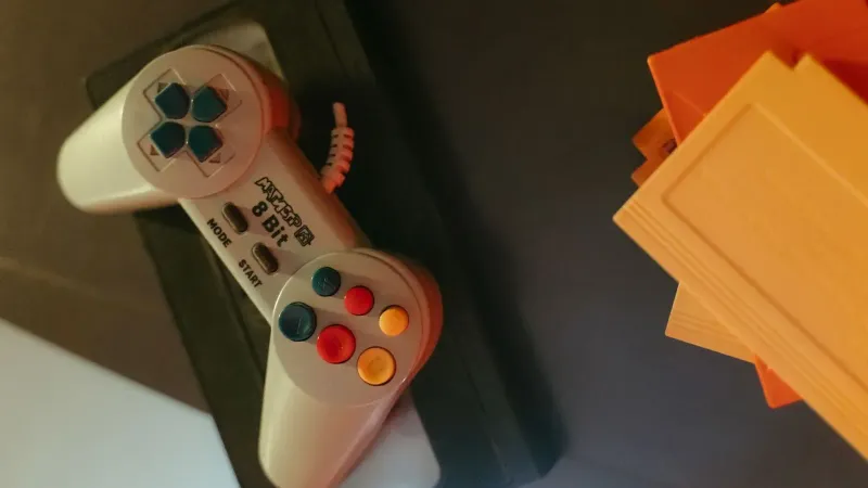 Un controlador de juego vintage de 8 bits con botones de colores junto a cartuchos de juegos clásicos.