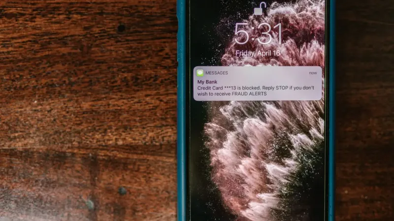 Close-up of smartphone displaying a fraud alert message on wooden surface.