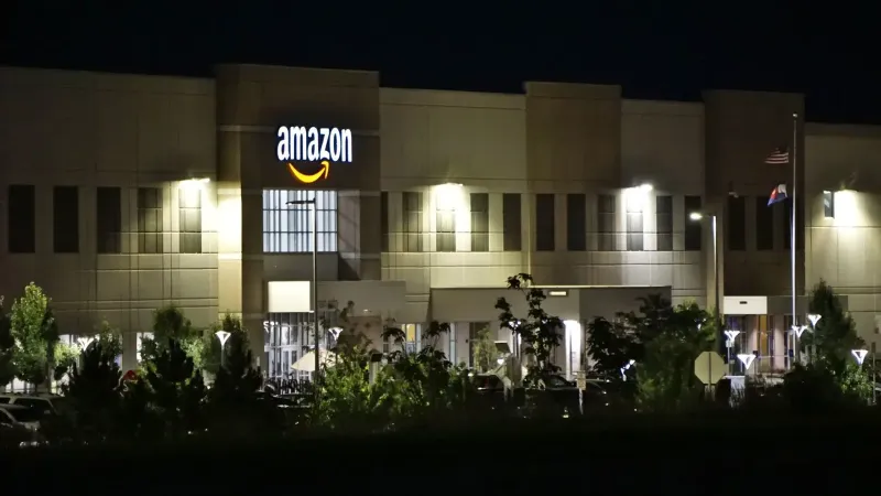 Edificio de almacén de Amazon iluminado por la noche con árboles y señalización.