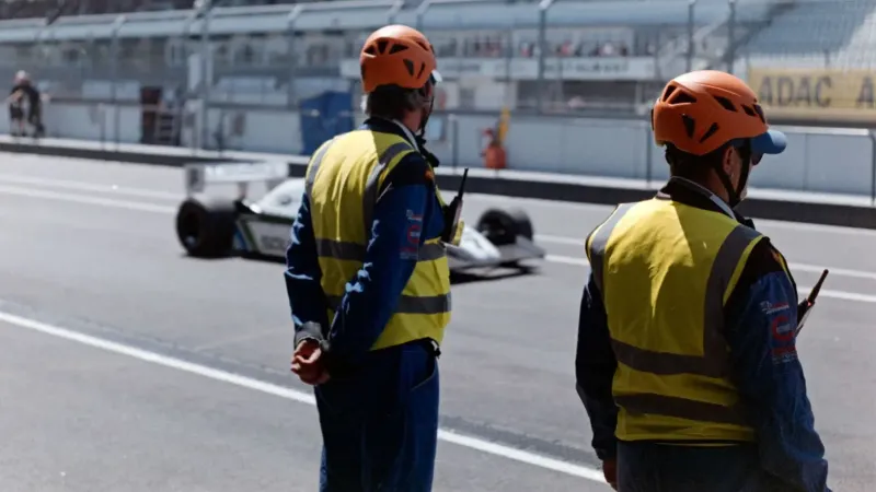 Dos oficiales de carrera en equipo de protección miran un automóvil en la pista de carreras en un evento de carreras.