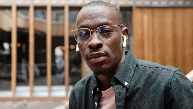 Hombre afroamericano calvo con gafas y auriculares, con una mirada segura, al aire libre.