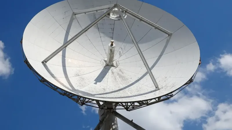 Una vista de ángulo bajo de una gran antena parabólica contra un cielo azul claro con nubes dispersas.