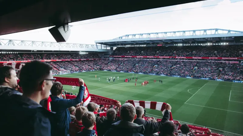 Fans cheer as players take the field at a vibrant football stadium, creating an electric atmosphere.
