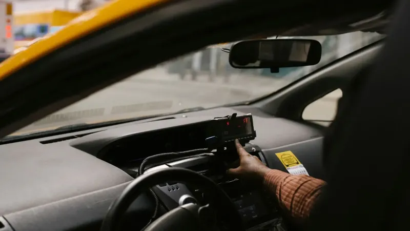 Conductor étnico masculino anónimo con volante usando el navegador GPS para buscar la dirección de conducción en la calle en la ciudad durante el trabajo