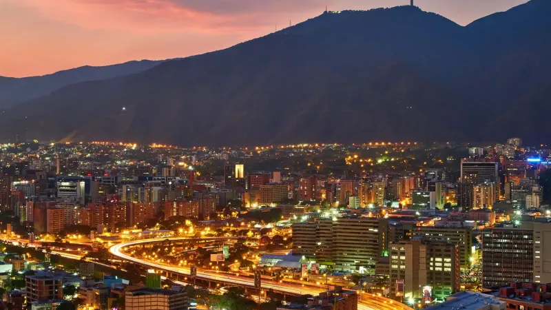 Una impresionante vista aérea del paisaje urbano de Caracas al anochecer, mostrando las vibrantes luces de la ciudad contra el telón de fondo montañoso.