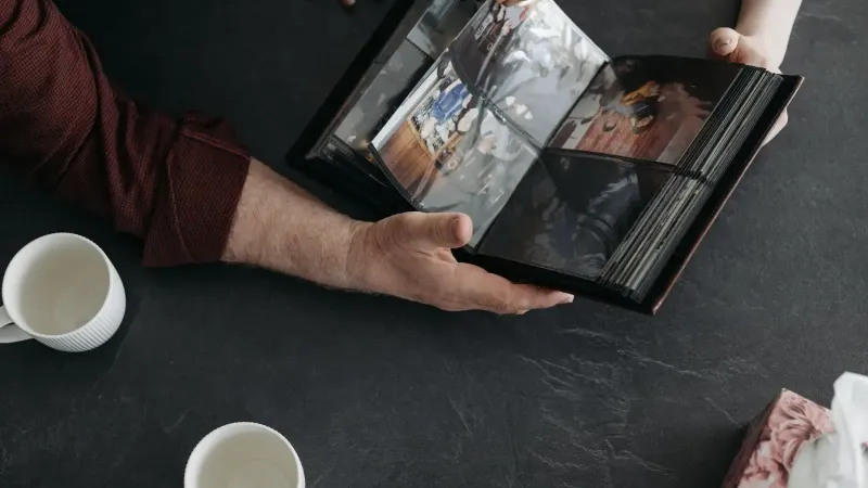 Hands holding a photo album with coffee cups, evoking memories and nostalgia.
