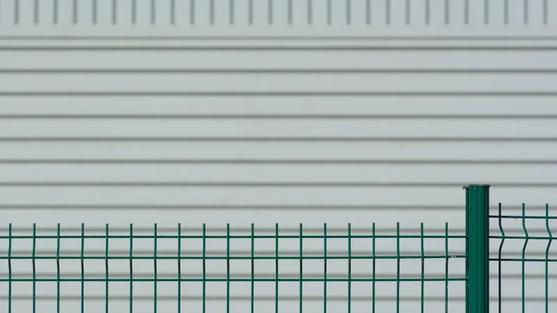 Valla de metal verde contrasta con una pared ondulada blanca, creando un patrón minimalista.