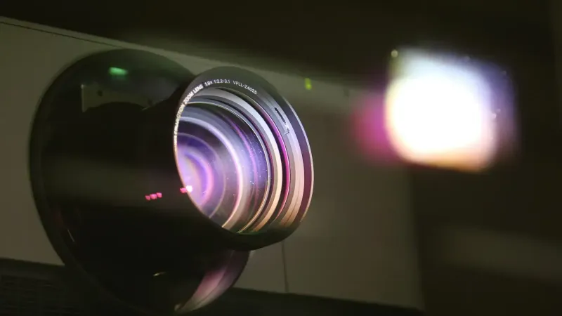 Vista detallada de una lente de proyector que emite luz, mostrando tecnología óptica.