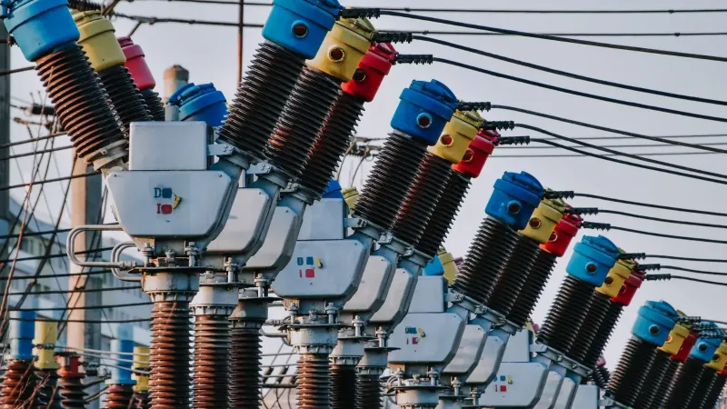 Close-up de transformadores eléctricos con tapas y cables coloridos en un entorno al aire libre.