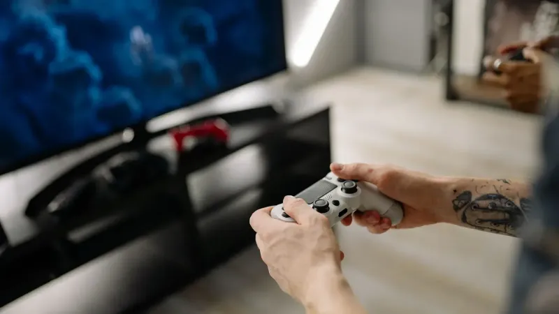 Persona jugando videojuegos usando un controlador de juego en interiores en una configuración de TV moderna.