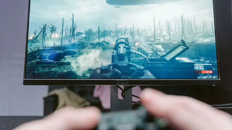 Una persona que juega un videojuego en un monitor de alta resolución, mostrando un paisaje de guerra.
