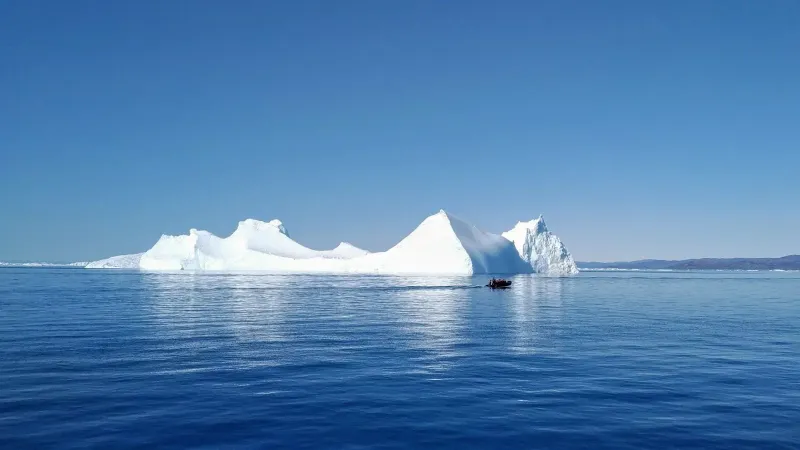 Una serena escena de un iceberg con un pequeño bote en las aguas de Ilulissat, Groenlandia.