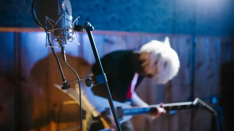 Blurred guitarist in a vibrant studio, mic in foreground capturing dynamic energy.