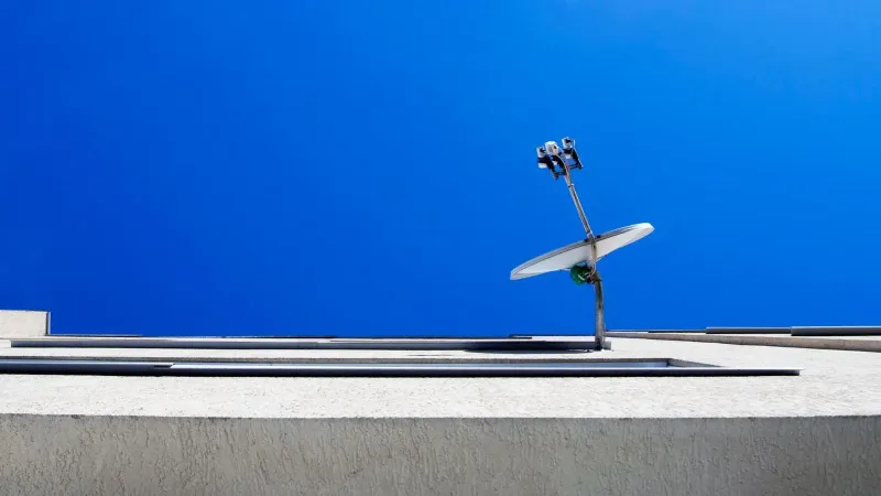 Vista de ángulo bajo de una antena parabólica en un edificio moderno contra un cielo azul claro.