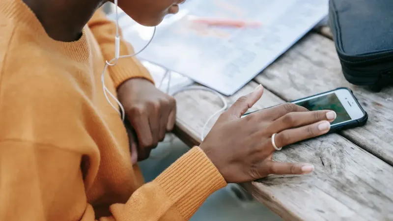 Desde arriba de la mujer afroamericana anónima recortar con auriculares usando teléfono móvil y mensajes de texto en la mesa