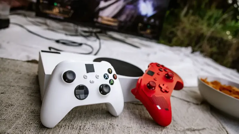 Controladores de juegos inalámbricos blancos y rojos en una superficie texturizada cerca de chips y una pantalla de TV.