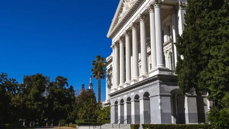 Beautiful sunlit view of the California State Capitol building with classic columns and vibrant blue sky.