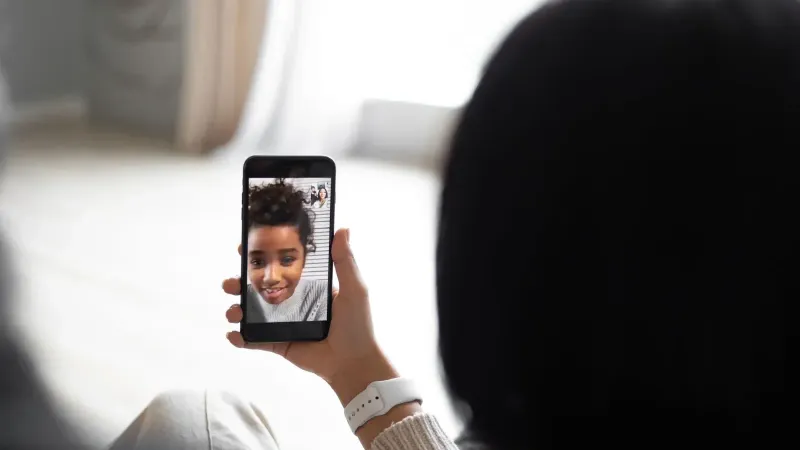Vista posterior de una pareja anónima comunicándose con un niño afroamericano a través de video chat en un teléfono inteligente moderno mientras se sienta en la sala de estar en un fondo