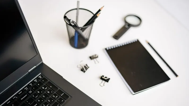 Un moderno espacio de trabajo de oficina con una computadora portátil, un cuaderno y papelería en un escritorio blanco.