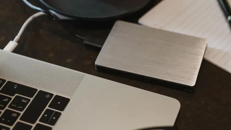 Primer plano de un disco duro externo conectado a una computadora portátil con un cable USB en un escritorio.