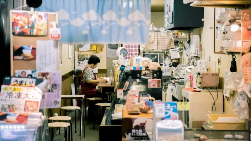 Cálido interior de una pequeña y acogedora tienda en Osaka, con una mujer asiática que trabaja, rodeada de productos locales y decoración.