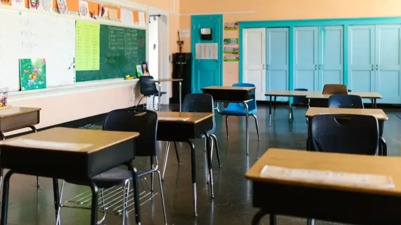 Aula vacía brillante y colorida con escritorios, pizarra y materiales educativos.