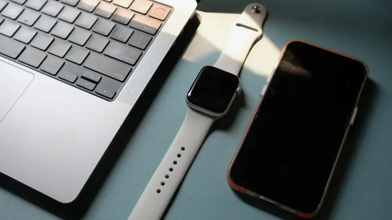 Flat lay of a laptop, smartwatch, and smartphone on a blue surface, highlighting modern technology.