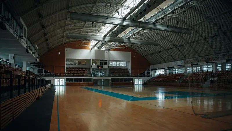 Arena deportiva interior vacía con pisos de madera dura y gradas, perfecta para diversas actividades deportivas.