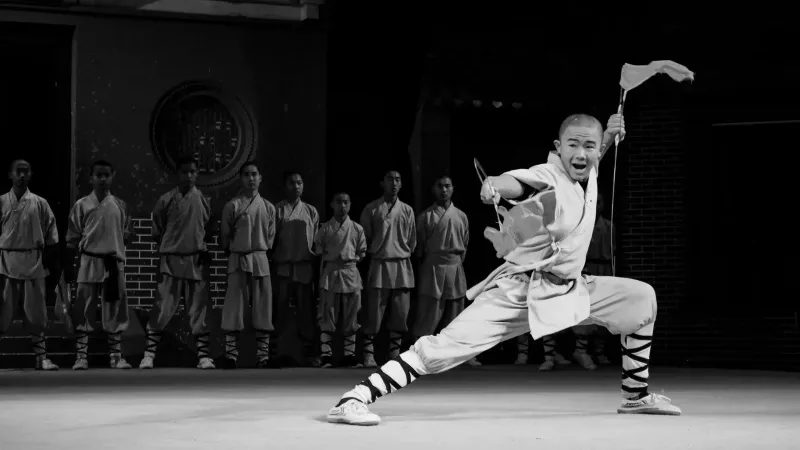 Artista marcial realiza una pose de kung fu enérgico en el escenario, rodeado de compañeros.