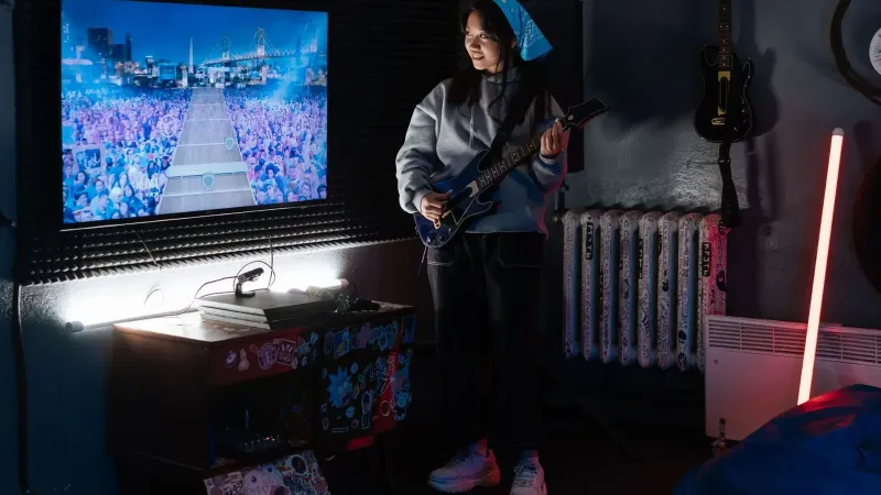 Asian woman enjoys a guitar video game in a cozy neon-lit room filled with music vibes.