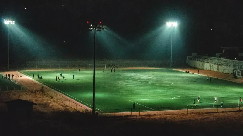 Un vibrante partido de fútbol nocturno en un estadio iluminado en Paro, Bhután, capturado desde un ángulo elevado.