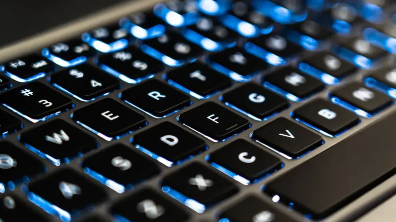 Detailed view of a backlit laptop keyboard keys with blue LED lighting for tech concepts.