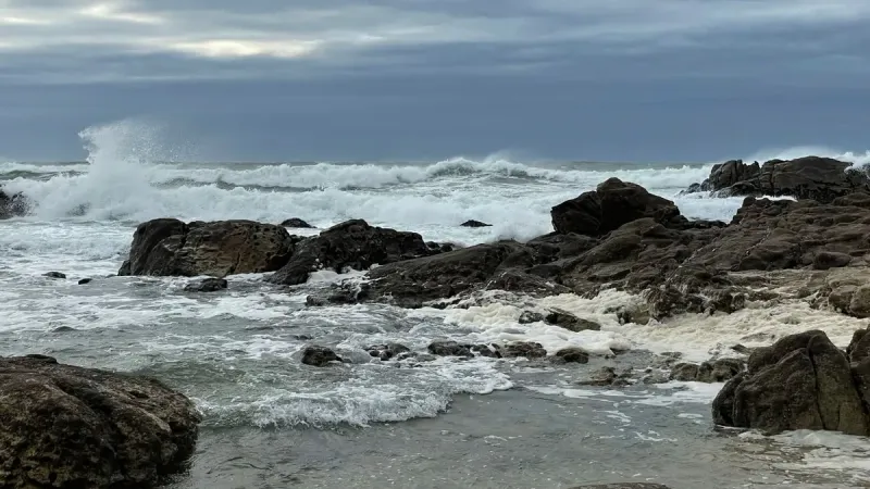 Paisaje marino rocoso con poderosas olas chocando contra la orilla bajo un cielo nublado.