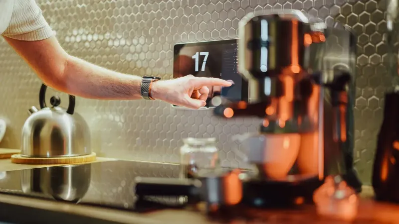 A man interacts with a touchscreen in a stylish kitchen setting, featuring modern appliances.