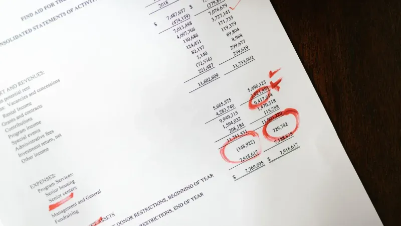 Estado financiero con anotaciones rojas sobre una mesa de madera.