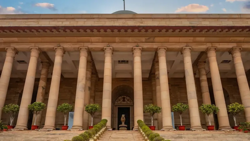 Edificio gubernamental en Nueva Delhi con columnas y una bandera india bajo un cielo vibrante.