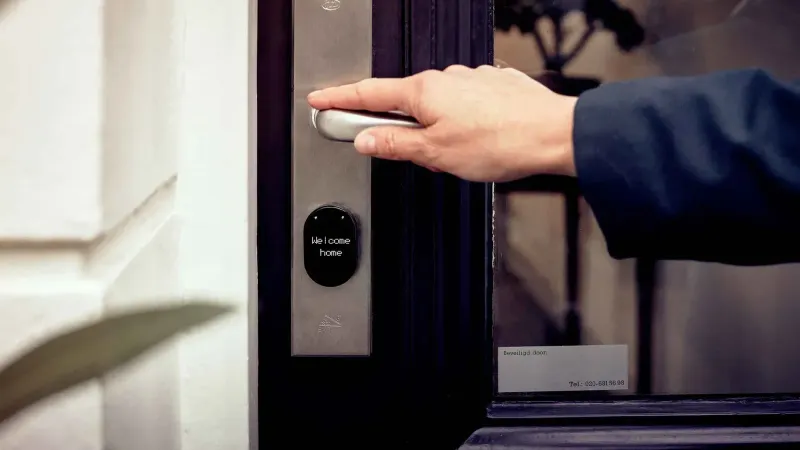 Una mano abriendo una puerta de casa inteligente con panel de acceso digital, transmitiendo seguridad y tecnología.