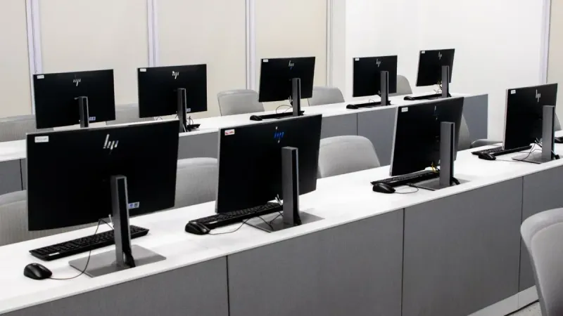 Un laboratorio de computadoras vacío con modernas configuraciones de escritorio y sillas ergonómicas.