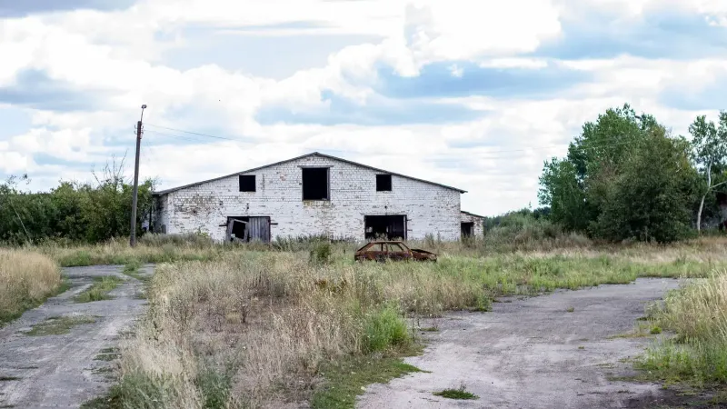 Antiguo almacén abandonado en una zona rural con césped cubierto y cielos nublados.